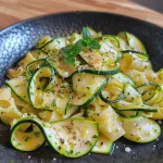 Nahaufnahme von Zucchini-Nudeln auf einem Teller mit Butter und Gewürzen.