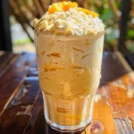 Nahaufnahme eines fruchtigen Mango-Kokosnuss-Milchshakes mit Sahne und Mangostückchen.