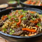 Nahaufnahme von Teriyaki-Rindfleischnudeln in einer weißen Schüssel.