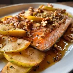 ['Close-up view of glazed salmon fillets topped with apple and onion slices.', 'Juicy salmon fillets drizzled with maple-mustard glaze and garnished with walnuts.', 'Salmon with a shiny glaze alongside thinly sliced apples and onions on a plate.', 'Colorful presentation of salmon dish featuring apples, onions, and walnuts.']