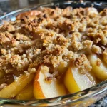 ['A close-up side view of a homemade pear crumble with a golden-brown topping.', 'Juicy pear crumble in a baking dish, showcasing a crunchy topping and sliced pears.', 'Side view of a delicious pear crumble with a crispy crust, highlighting the fruit filling.', 'Close-up of a freshly baked pear crumble with a rich, buttery top and visible slices of pear.']