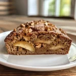 ['A close-up side view of freshly baked pear bread topped with walnuts.', 'Sliced pear bread showcasing its moist texture and chunks of pear and nuts.', 'A golden-brown loaf of pear bread with visible ingredients and a rustic appearance.', 'A detailed view of a slice of pear bread highlighting the juicy pear pieces and spices.']