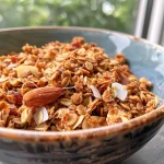 ['Close-up of Easy Maple Cinnamon Granola in a bowl, showcasing oats and spices.', 'Side view of granola mix featuring rolled oats, coconut, and a cinnamon dusting.', 'Detailed image of homemade granola with visible ingredients like oats and nuts.', 'Textured granola mix with an emphasis on golden oats and a sprinkle of cinnamon.']