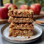 ['Close-up view of spiced apple oat squares with a golden-brown crust and visible apple chunks.', 'Deliciously baked apple and oat squares showcasing a rich, caramelized top and soft texture.', 'Side view of fresh apple oat squares dotted with cinnamon and nutmeg, arranged on a wooden board.', 'Tasty spiced apple oat squares featuring diced apples and a sprinkle of cinnamon, ready to serve.']