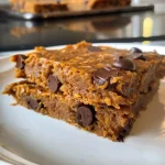 ['Close-up of gluten-free pumpkin oatmeal cookies with chocolate chips.', 'Side view of freshly baked gluten-free pumpkin cookies with a golden-brown texture.', 'Juicy gluten-free pumpkin oatmeal cookies highlighting chocolate chips and oats.', 'Delicious pumpkin oatmeal cookies displayed on a surface, showcasing their ingredients.']