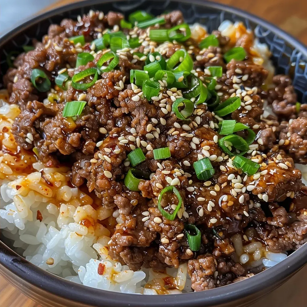['A close-up view of a Korean Ground Beef Bowl with vibrant colors and textures.', 'Juicy ground beef served over a bed of rice with garnishes.', 'A side view of a bowl filled with Korean-style ground beef, rice, and fresh toppings.', 'An appetizing close-up of a Korean beef bowl showcasing toppings and ingredients.']