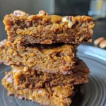 ['A close-up view of golden-brown pumpkin pecan cookies with chopped pecans sprinkled on top, showcasing their soft texture.', 'Side view of a stack of freshly baked pumpkin pecan cookies, highlighting their vibrant orange color and nutty surface.', 'Detailed side perspective of pumpkin pecan cookies, featuring a glossy sheen from the coconut oil and a scattering of pecans.', 'Close-up shot of a single pumpkin pecan cookie, emphasizing its chewy texture and warm spices against a soft background.']