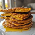 ['Close-up view of golden pumpkin pancakes topped with cottage cheese and maple syrup.', 'Side view of fluffy pumpkin pancakes stacked on a plate, garnished with cottage cheese.', 'Delicious pumpkin pancakes drizzled with syrup and served with a side of cottage cheese.', 'Juicy pumpkin pancakes, visibly textured, with a dollop of cottage cheese beside them.']