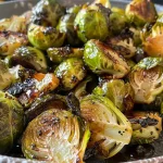 ['Close-up view of glossy Brussels sprouts drizzled with maple glaze.', 'Roasted Brussels sprouts coated in a shiny maple syrup glaze.', 'Side view of Brussels sprouts glistening with a sweet glaze on a plate.', 'Fresh Brussels sprouts with a caramelized maple finish displayed attractively.']