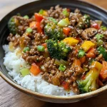 ['A close-up view of a vibrant stir-fry bowl featuring ground beef, colorful veggies, and rice.', 'A side view of a delicious beef stir-fry bowl with garlic-seasoned vegetables and steamed rice.', 'A hearty bowl of spicy ground beef stir-fry with broccoli, bell peppers, and zucchini.', 'A succulent stir-fry bowl with rich ground beef, garlic vegetables, and a bed of white rice.']