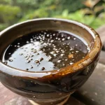 Close-up of a glossy balsamic glaze in a small bowl with ingredients beside it.