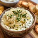 Close-up of creamy caramelized onion dip in a bowl with chives on top.