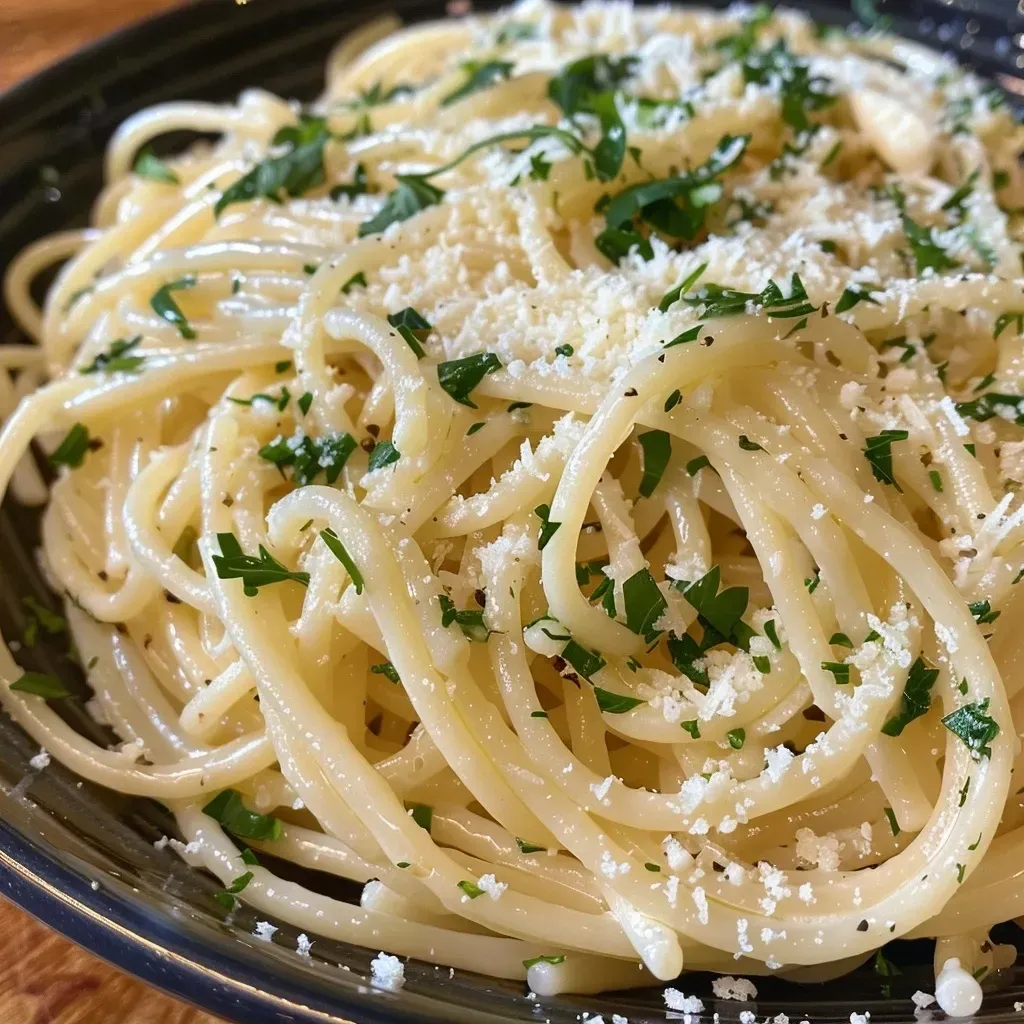 Side shot of angel hair pasta coated in garlic butter and sprinkled with grated Parmesan cheese.