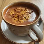 Close-up of a creamy pumpkin spice hot chocolate topped with whipped cream and cinnamon.