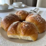 Close-up side view of golden-brown milk bread dinner rolls on a rustic wooden surface.