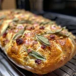 Close-up of a loaf of sage, speck, and garlic pull-apart bread with golden crusts and visible garlic cloves.